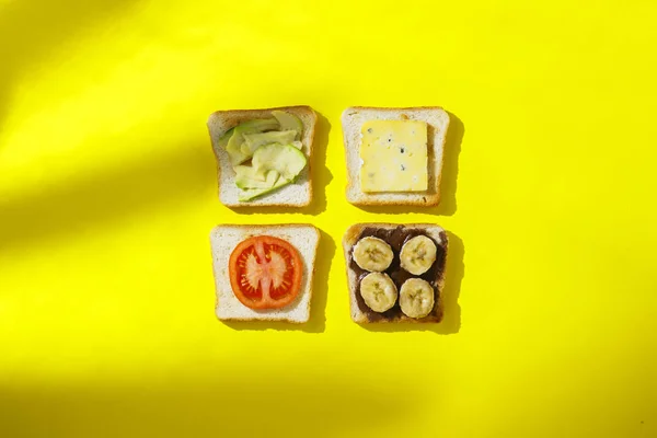 Sandwiches mit Banane, Tomate, Avocado, Blauschimmelkäse auf gelbem Hintergrund. Konzept eines gesunden Frühstücks, Vitamine, richtige Ernährung. natürliches Licht, Schatten von Pflanzen. flache Lage, Draufsicht. — Stockfoto