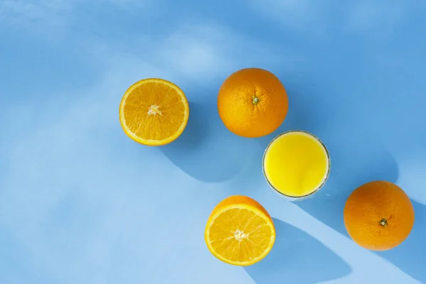Un vaso de jugo de naranja y naranjas sobre un fondo azul. Concepto de vitaminas, trópico, verano. Luz natural. Piso tendido, vista superior . — Foto de Stock