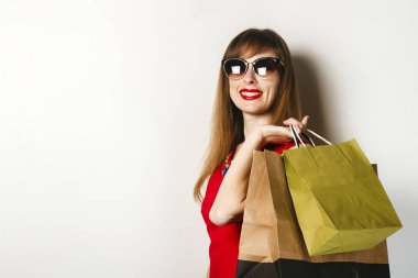 Kırmızı elbiseli genç bir kız, hafif bir arka plan üzerinde alışveriş yaptıktan sonra elinde paketleri tutar. Konsept satış, alışveriş.