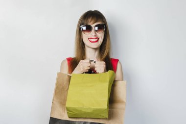 Kırmızı elbiseli genç bir kız, hafif bir arka plan üzerinde alışveriş yaptıktan sonra elinde paketleri tutar. Konsept satış, alışveriş.