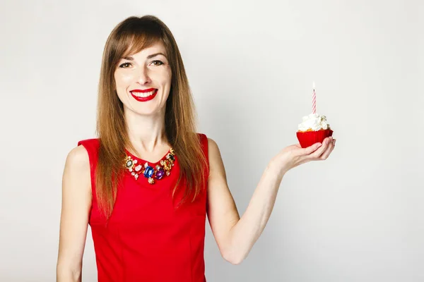 빨간 드레스를 입은 한 소녀가 밝은 배경에 촛불이 달린 컵케이크를 들고 있다. 생일 축 하 컨셉. — 스톡 사진