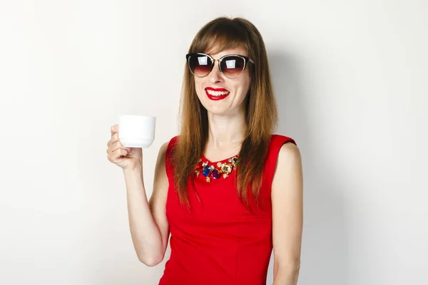 Una joven con un vestido rojo sostiene en su mano una taza de café sobre un fondo claro. concepto de cafetería, desayuno . — Foto de Stock