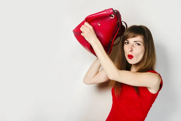 Una joven con un vestido rojo está protegida por una bolsa sobre un fondo claro. El concepto de un ataque a una chica, protección contra un ladrón, gángster . — Foto de Stock