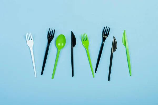 Disposable plastic tableware and appliances for food on a blue background. Fork, spoon and knife. Concept plastic, harmful, environmental pollution, stop plastic. Flat lay, top view.