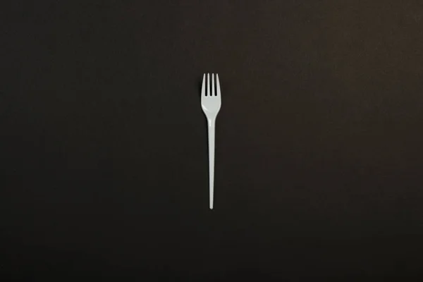 White plastic fork on a black background. Concept plastic, harmful, environmental pollution, stop plastic. Flat lay, top view. — ストック写真