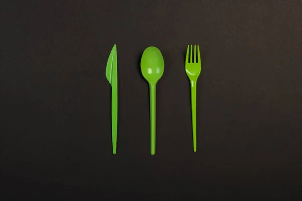 Green Disposable plastic tableware and appliances for the food on a black background. Fork, spoon and knife. Concept plastic, harmful, environmental pollution, stop plastic. Flat lay, top view.