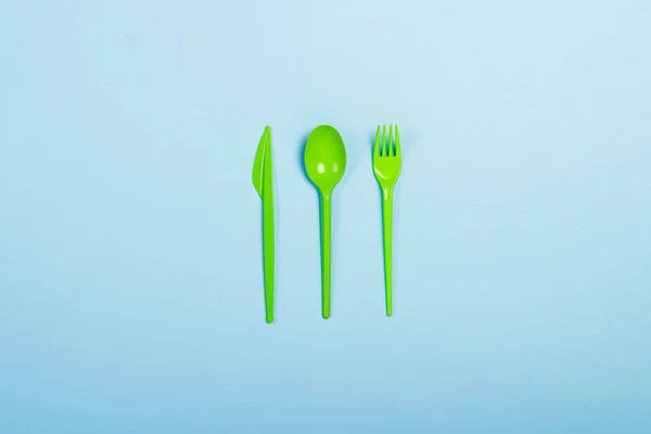 Green Disposable plastic tableware and appliances for food on a blue background. Fork, spoon and knife. Concept plastic, harmful, environmental pollution, stop plastic. Flat lay, top view.
