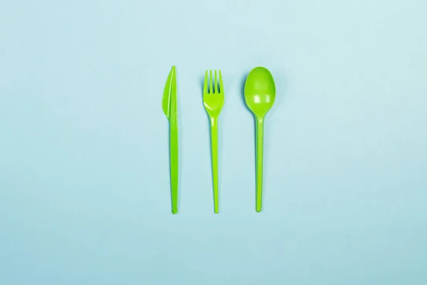 Green Disposable plastic tableware and appliances for food on a blue background. Fork, spoon and knife. Concept plastic, harmful, environmental pollution, stop plastic. Flat lay, top view.