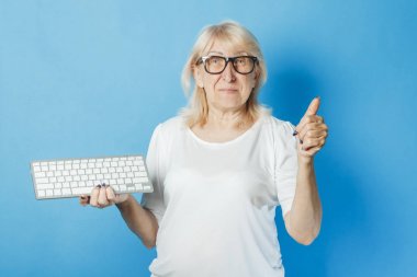Gözlüklü yaşlı bir bayanın mavi arka planda klavyesi var. Yaşlılar için internet konsepti, yeni teknolojiler, yaşlılar tarafından bilgisayar öğrenimi, teknoloji