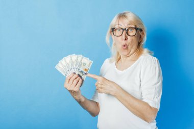 Old lady with glasses holds money in her hands against a blue background. Concept of wealth, winnings, savings, lottery, loan clipart