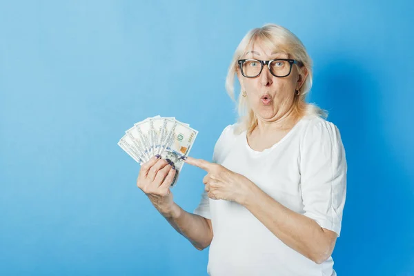 Eine alte Dame mit Brille hält vor blauem Hintergrund Geld in der Hand. Konzept des Reichtums, Gewinne, Ersparnisse, Lotterie, Darlehen — Stockfoto