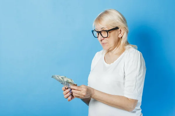 Old lady with glasses holds money in her hands against a blue background. Concept of wealth, winnings, savings, lottery, loan — Stock Photo, Image