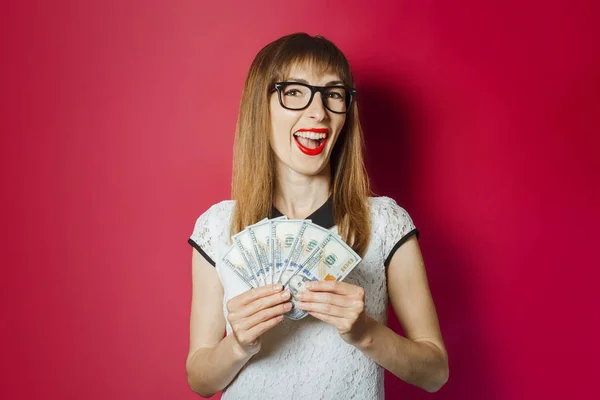 Junge Frau hält Geld auf dunkelrotem Hintergrund. Konzept reich, Gewinne, Lotterie, Kredit, Bestätigung — Stockfoto