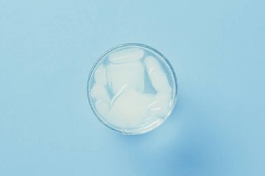 Mavi arka planda bir bardakta buzla canlandırıcı soğuk su. 