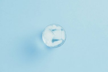 Mavi arka planda bir bardakta buzla canlandırıcı soğuk su. 