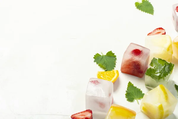 Ice cubes with fruit and mint leaves on a white stone background — Stock Photo, Image