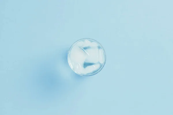 Água fria refrescante com gelo em um copo em um fundo azul . — Fotografia de Stock