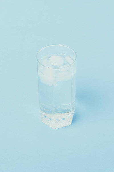 Refreshing cold Water with ice in a glass on a blue background. 