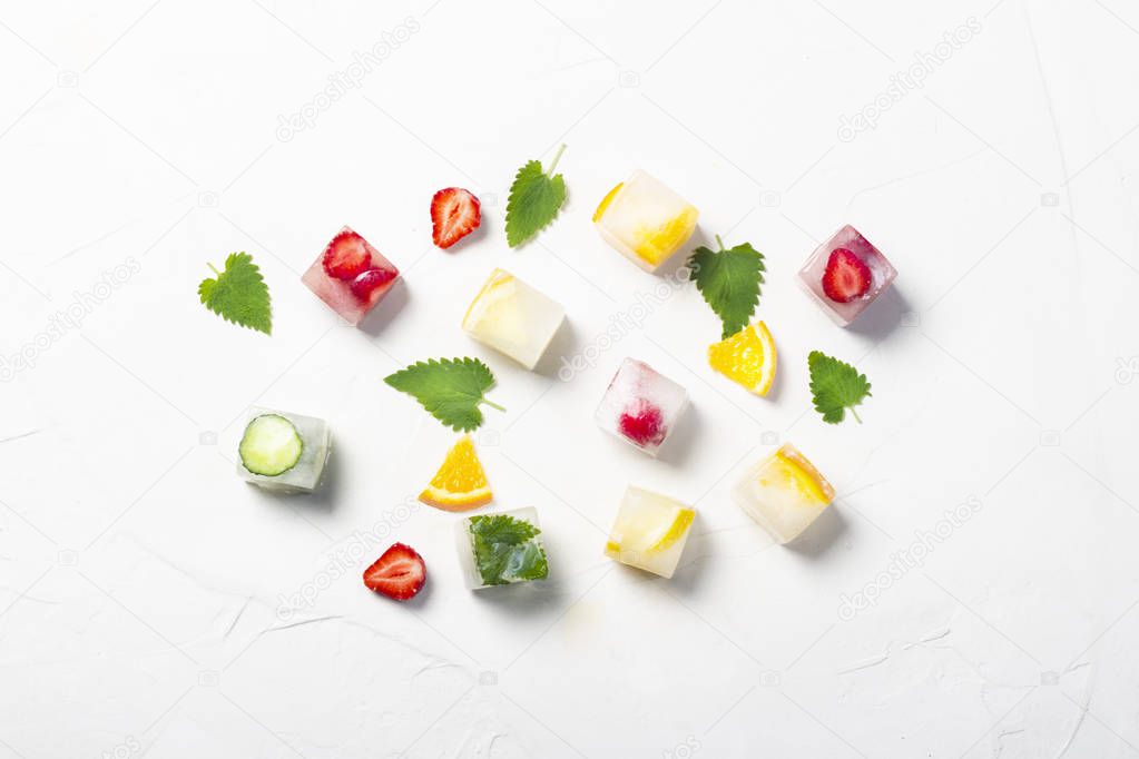 Ice cubes with fruit and mint leaves on a white stone background