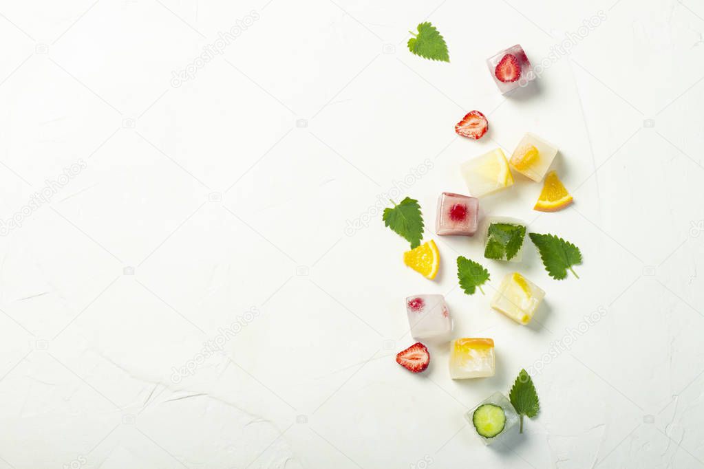Ice cubes with fruit and mint leaves on a white stone background