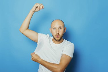 Mavi arka planda terden sırılsıklam olmuş beyaz tişörtlü genç bir adam. Aşırı terleme, ısı, deodorant kavramı