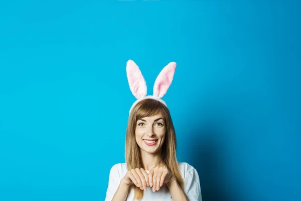 A young woman in the ears of a bunny smiles on a blue background. Easter concept — Stock Photo, Image