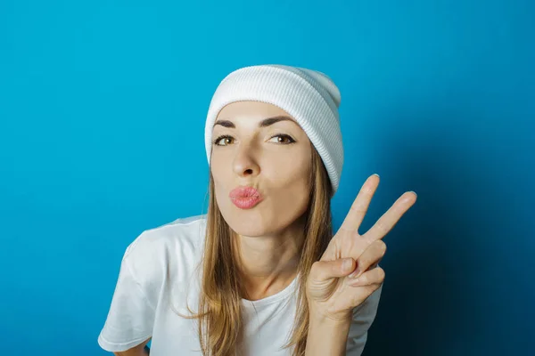 Mujer joven con sombrero blanco y camiseta hace un gesto de mano sobre un fondo azul — Foto de Stock