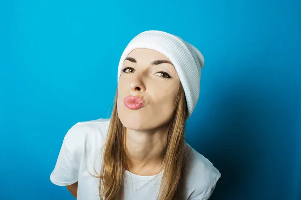 Mujer joven con un sombrero blanco y una camiseta con una cara sorprendida sobre un fondo azul — Foto de Stock