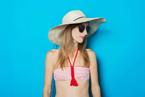 Jonge vrouw in een badpak, bril en een hoed met een brede rand op een blauwe achtergrond. Concept van vakantie, zomer, vakantie op zee — Stockfoto