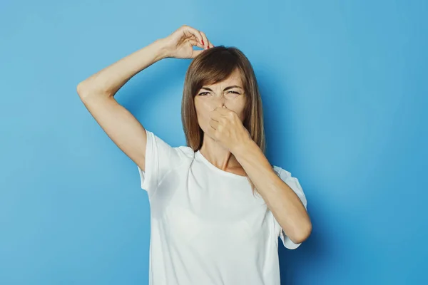 Menina nova em uma camiseta branca com axilas molhadas do suor em um fundo azul. Conceito de transpiração excessiva, calor, desodorizante — Fotografia de Stock