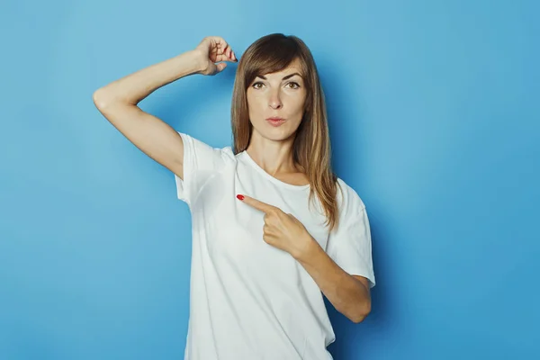Chica joven con una camiseta blanca muestra un dedo en las axilas mojadas del sudor sobre un fondo azul. Concepto de sudoración excesiva, calor, desodorante — Foto de Stock