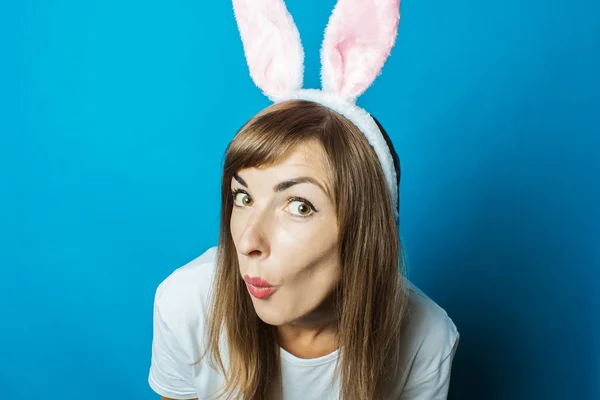 Mujer joven en orejas de conejo con una cara sorprendida sobre un fondo azul. Concepto Pascua — Foto de Stock