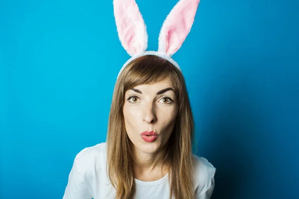 Mujer joven en orejas de conejo con una cara sorprendida sobre un fondo azul. Concepto Pascua — Foto de Stock