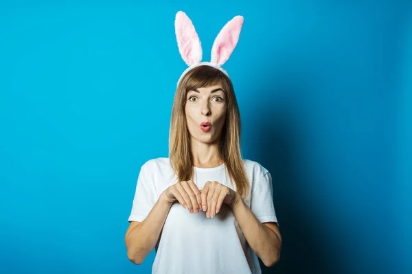 Young woman in bunny ears with a surprised face on a blue background. Easter concept — Stock Photo, Image