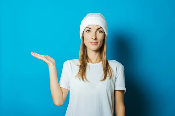 Młoda kobieta w białym kapeluszu i t-shirt sprawia, że gest ręka na niebieskim tle — Zdjęcie stockowe