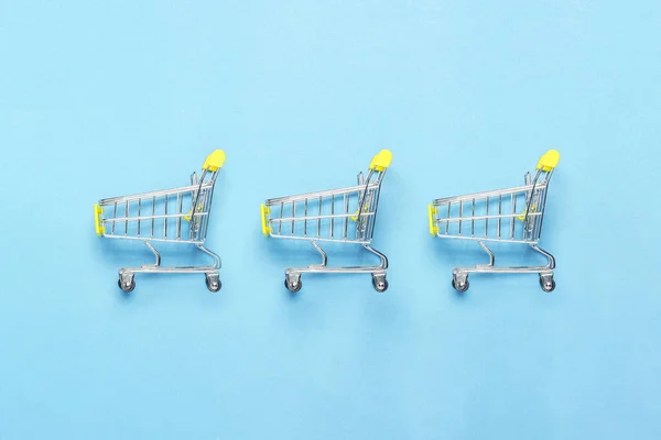 Drei Einkaufswagen auf blauem Hintergrund. Konzept von Einkaufen, Rabatt, Verkauf. flache Lage, Draufsicht — Stockfoto