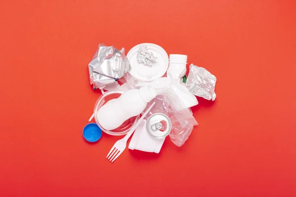 Plastic and tin waste collection on a red background. Concept stop plastic, recycling, separate collection of garbage. Flat lay, top view