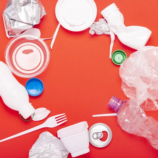 Plastic and tin waste collection on a red background. Concept stop plastic, recycling, separate collection of garbage. Circle shape. Flat lay, top view