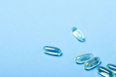 Mavi arka plandaki kapsüller. Vitamin kavramı, balık yağı, ilaç, ilaç, ilaç endüstrisi. Düz döşeme, üst görünüm