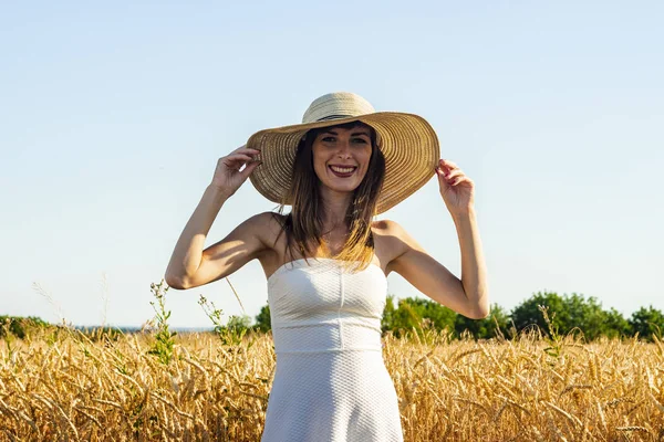 Joven mujer hermosa con un vestido blanco y un sombrero en el campo de una milf. El concepto de recreación al aire libre, un viaje al pueblo — Foto de Stock
