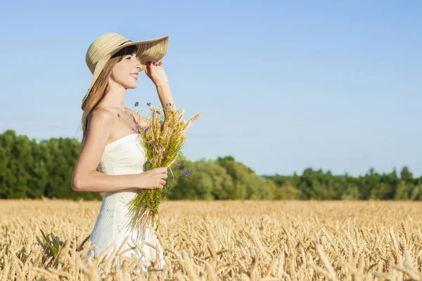 Młoda piękna kobieta w białej sukience i kapeluszu posiada bukiet z dzikimi kwiatami na polu prosa. Koncepcja rekreacji na świeżym powietrzu, wycieczka do wsi — Zdjęcie stockowe