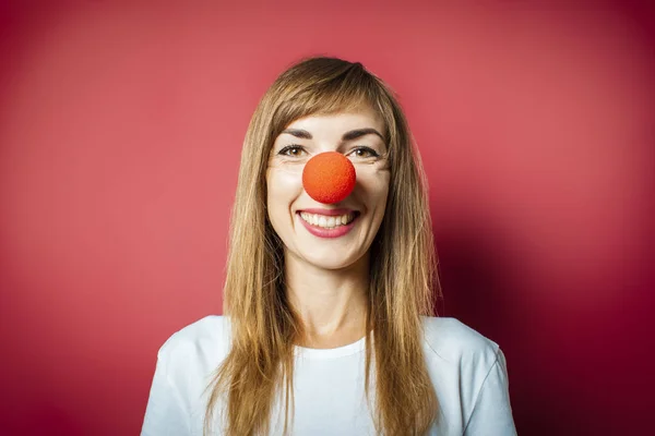 Young beautiful woman with a red nose of a clown on a pink background. Concept red nose day, holiday, party, clown