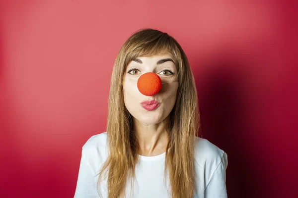 Joven mujer hermosa con una nariz roja de un payaso sobre un fondo rosa. Concepto nariz roja día, fiesta, fiesta, payaso — Foto de Stock