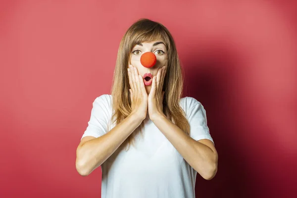 Funny young woman with a red nose of a clown on a pink background. Concept red nose day, holiday, party, clown — Stock Photo, Image