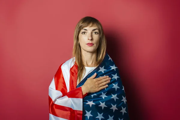 Young girl holds the US flag on a pink background. Concept patriot, holiday, independence day, memorial day, US visa, emigration to USA, education in USA