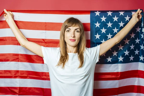 Young girl holds the US flag on a pink background. Concept patriot, holiday, independence day, memorial day, US visa, emigration to USA, education in USA