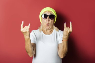 Şapkalı komik yaşlı kadın, pembe bir arka plan üzerinde el hareketi yapıyor. Konsept serin şık büyükanne, modern stil