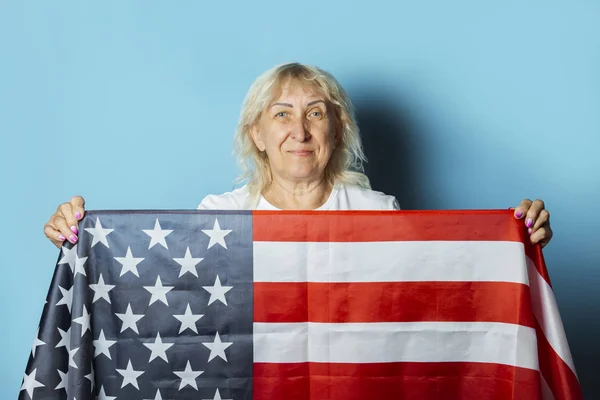 Old woman holds American flag on a blue background. Independence Day celebration concept, memorial day, emigration, US flag