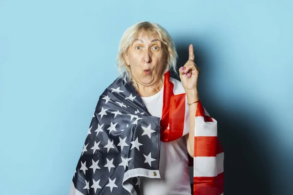 Old woman holds US flag on a blue background. Independence Day celebration concept, memorial day, emigration