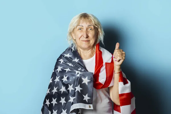 Old woman holds American flag on a blue background. Independence Day celebration concept, memorial day, emigration, US flag